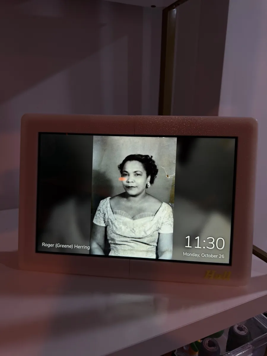 The photo frame on a shelf, showing a black-and-white family portrait with a name caption in the lower left and the time and date in the lower right.